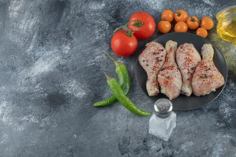 Top view. Raw chicken drumstick on black plate with fresh vegetables. Stock Photos