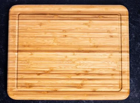 Top view of a rectangular wooden chopping board on the dark-colored surface 库存照片