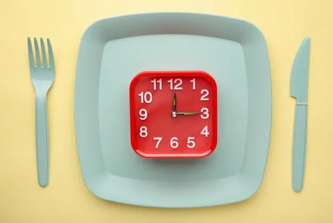 Top view of red alarm clock with plate, fork and knife on yellow background - Foto stock