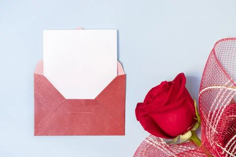 Top view of red envelope and white empty card with beautiful rose on light blue Фото