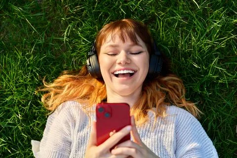 Top view red-haired young female in headphones with smartphone, on green grass Stock Photos