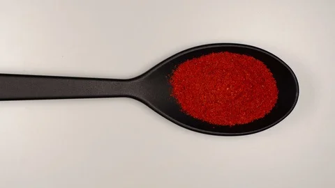 TOP VIEW: Red pepper powder fill a black plastic spoon on a table - Stop motion Stock Footage 124623228