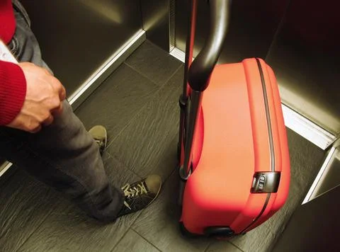 Top view of red plastic suitcase and lower body of a young man in elevator Stock Photos