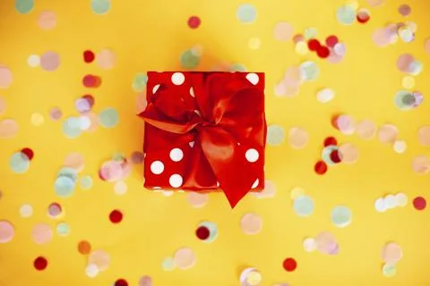 Top view of red polka dot gift box with ribbon placed on yellow surface Stock Photos