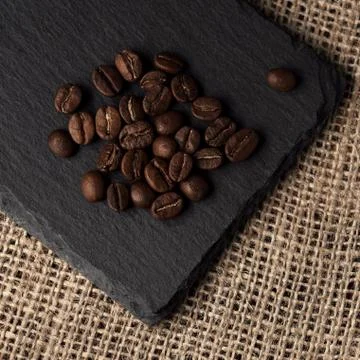 Top view of roasted coffee bean heap on black plate on hessian sack textile w Stock Photos