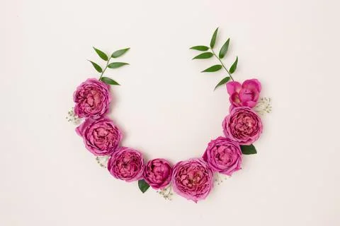 Top view of round frame made of rose and green leaves on a beige background. Stock Photos