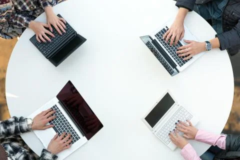 Top View of Rounded Desk with Four Laptops and People Hands Typing Stock Photos