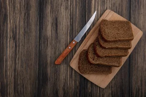Top view of rye bread slices on cutting board and knife on wooden backgroun.. Фото