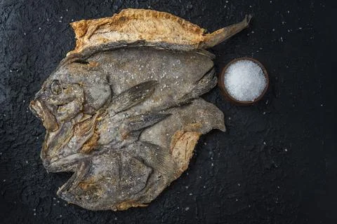 Top view of salted cod on a black stone background with grains of sea salt Stock Photos