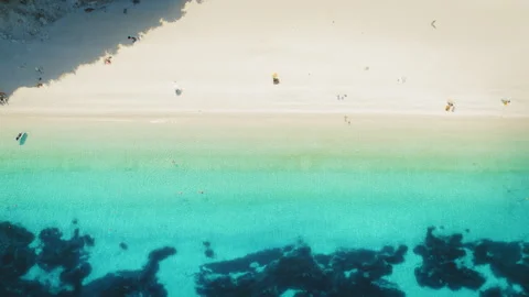 Top view of a sandy beach with people relaxing near clear shallow waters in Stock Footage 312653654