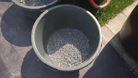 Top view: A shovel pours gray gravel into a large black bucket. Stock Footage 341400507