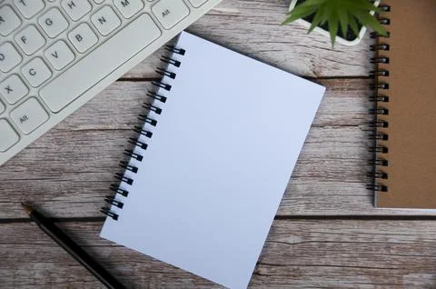 Top view of simple office desk with computer keyboard, pen and blank notepad. Stock Photos
