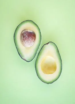 Top view of single avocado cut in half on solid green background. Stock Photos