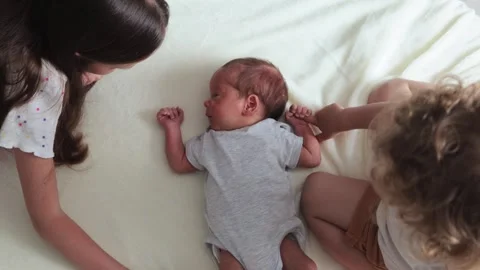 Top view of sisters in their casual outfits gently stroking their baby brother's Видео 291412209