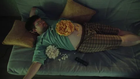 Top view of sleeping man on sofa with pillows, chips on his naked stomach Stockbeeldmateriaal 314396705