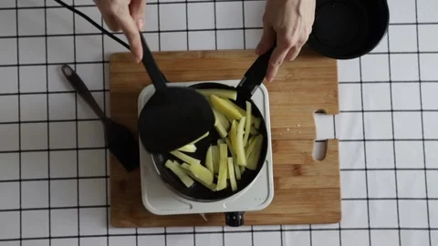 Top view of sliced raw potatoes frying in a black pan on a stove with a spa.. Stock Footage 316549468
