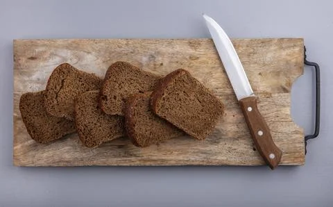 Top view of sliced rye bread and knife on cutting board on gray background Фото