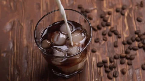 Top view Slow motion of cream being poured into a glass of cold brew iced coffee Stock Footage 128423633