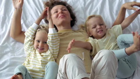 Top view slow motion happy cheerful woman with children on bed dangling their Stock Footage 242065111