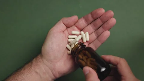 Top view slow motion of man pouring pills from bottle into palm on green Stock Footage 343450035