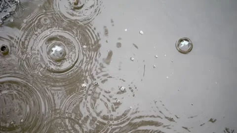 Top view of slow raindrops entering a puddle; bubbles rise, water mirrors t.. Video stock 255277859