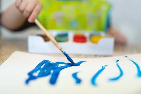 Top view of the small child is drawing with bright paints on paper, close up. Stock Photos