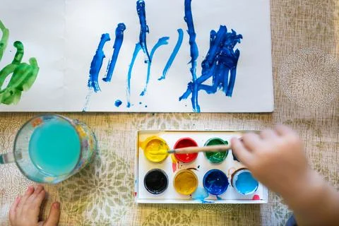 Top view of the small child is drawing with bright paints on paper, close up. Stock-Fotos