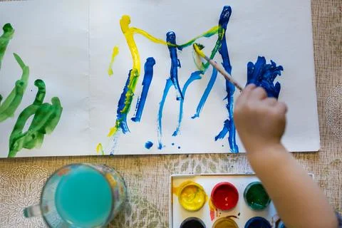 Top view of the small child is drawing with bright paints on paper, close up. Stock Photos