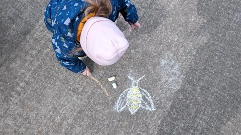 Top view of a small child drawing a bee with chalk on rough pavement, with pa 스톡 사진