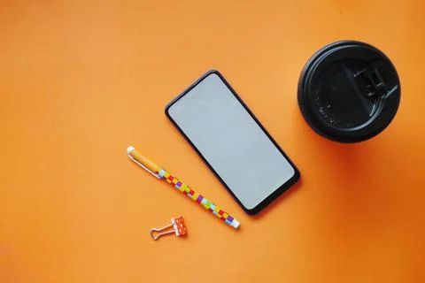 Top view of smart phone, tea cup and pen on orange background Stock Photos