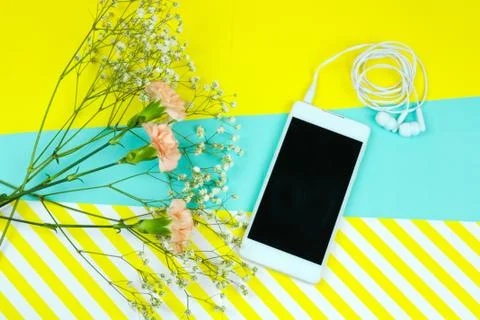 Top view smartphone with earphones and flowers on a vibrant  blue and strippe Stock Photos
