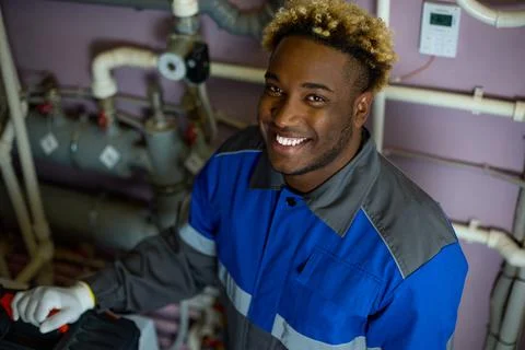Top view of a smiling black worker in overalls standing in the boiler room Stock Photos