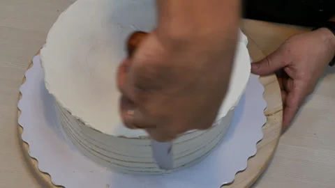 Top view smoothing the cream on a biscuit round cake with a special spatula Stock Footage 162176153