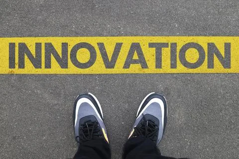 Top view of sneakers standing on asphalt behind a yellow line with INNOVATI.. Stock Photos