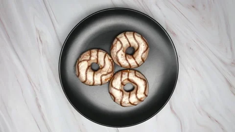 Top View Spinning Donuts Covered In White Frosting With Brown Swirls On A Black  Vídeo Stock 150090628