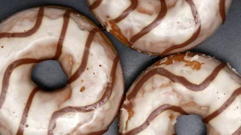 Top View Spinning Donuts Covered In White Frosting With Brown Swirls On A Black  Stock Footage 150278808