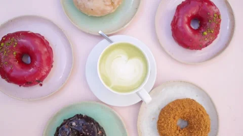 Top view of spinning image of matcha latte surrounded by colorful donuts. Stock Footage 139685328