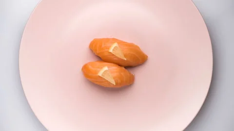 Top view of spinning two salmon sushi with lemon slices on the spinning pink Stock Footage 127107795