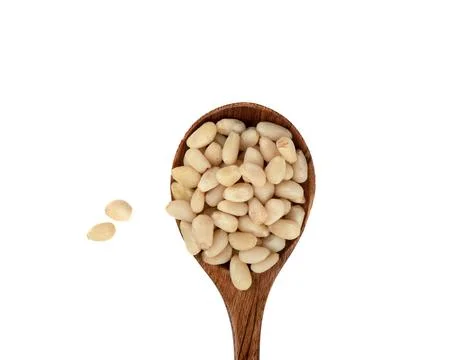 Top view of a spoon with peeled pine nuts on a white background. Stock Photos