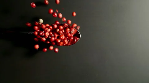 TOP VIEW: Spoon with pink pepper seeds fall on black table. Slow motion, Splash. Видео 142914408