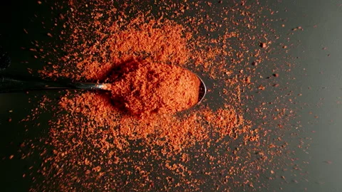 TOP VIEW: Spoon with red pepper powder fall on black table. Slow motion, Splash. Stock Footage 142914464
