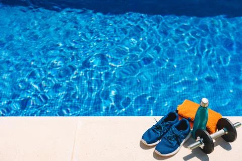 Top view of sports objects in front of a swimming pool. orange towel, blue water Stock Photos