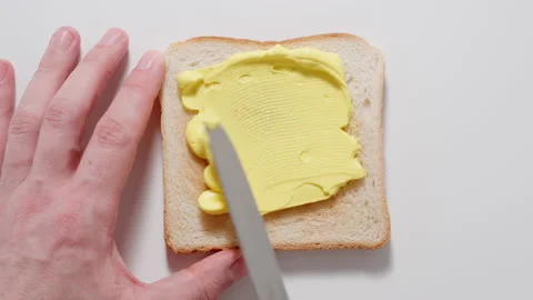 TOP VIEW: Spreading yellow paste on a toast with knife. Vídeo Stock 144417144