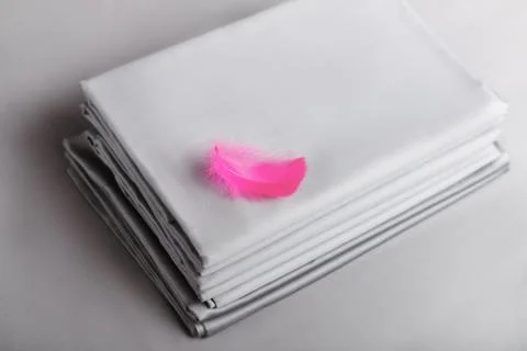 Top view of a stack of folded bedsheets of gray color with a pink feather. Stock Photos