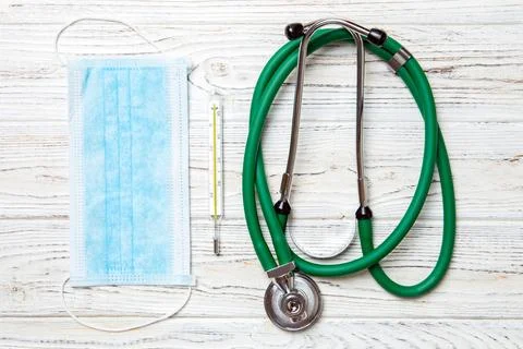 Top view of stethoscope, protective mask and mercury thermometer on white woo Stock Photos
