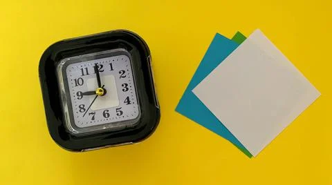Top view of sticky note and alarm clock with yellow color background. Stock Photos