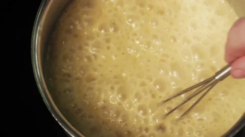 TOP VIEW of stirring with a whisk boiling yellow cream soup in a saucepan Stock Footage 138190832