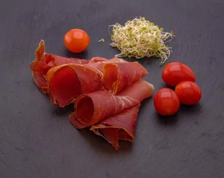 Top view on stone table with jamon , cherry tomatoes and alfalfa sprouts. Stock Photos