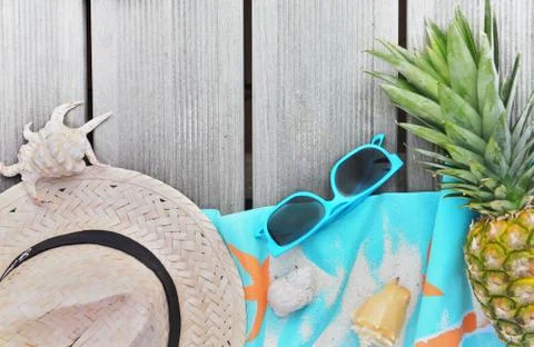 Top view on straw hat, beach towel, sunglasses and pineapple on wooden terrac Stock Photos