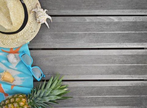 Top view on straw hat, beach towel, sunglasses and pineapple on wooden terrac Stock Photos
